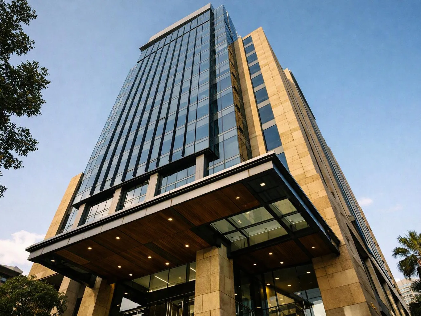 A tall glass office tower rises above a wood-paneled entrance against a clear blue sky